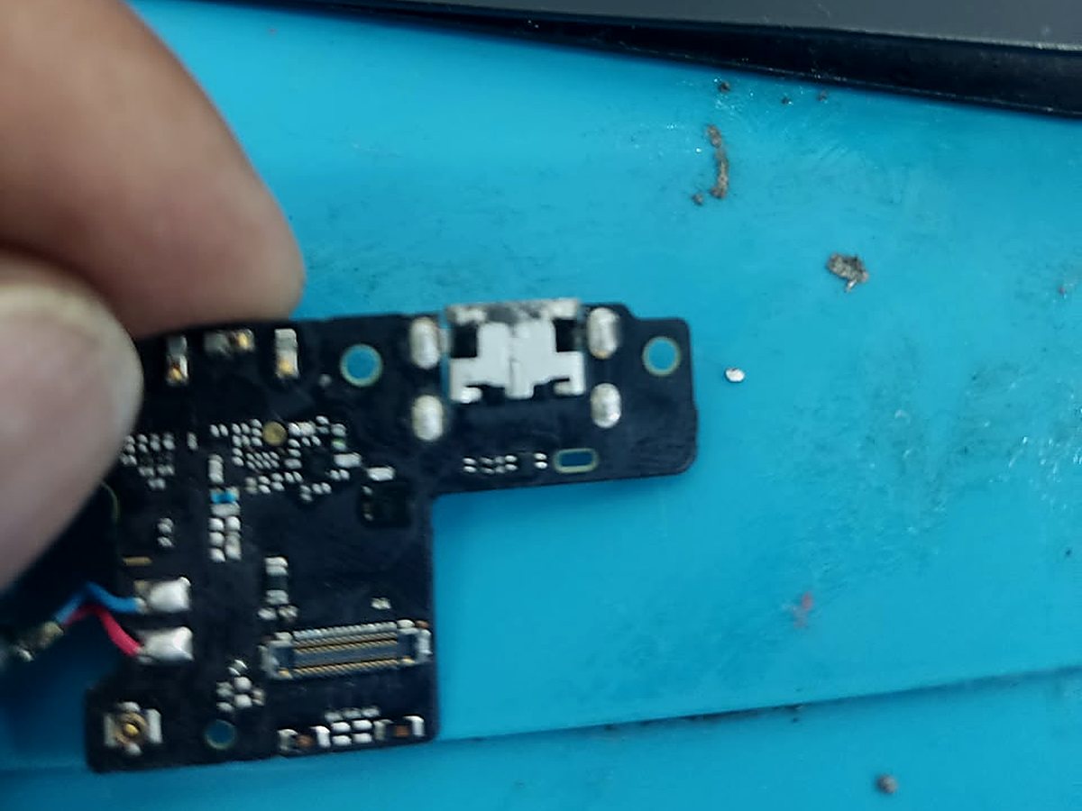 Placa del zócalo de carga de un celular sostenida con los dedos